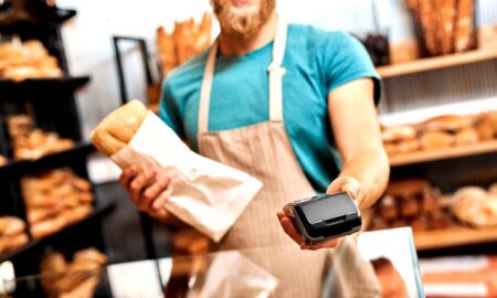 Sprzedawca w piekarni trzymający w jednej ręce chleb, a w drugiej terminal płatniczy